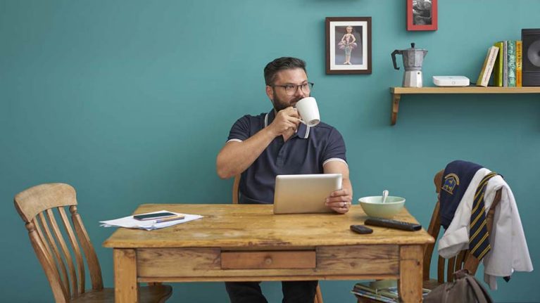 Image of a home worker drinking tea and using his laptop