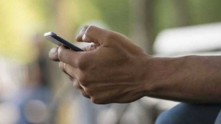 The hands of a person sending a text message on their EE Business phone in front of a blurred background. 