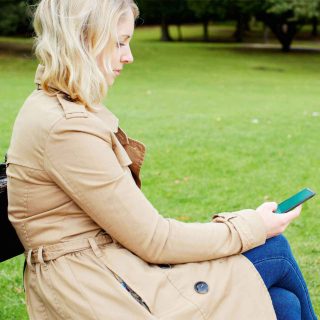 A woman looking at the screen of her EE Business phone while sitting outside on a bench.