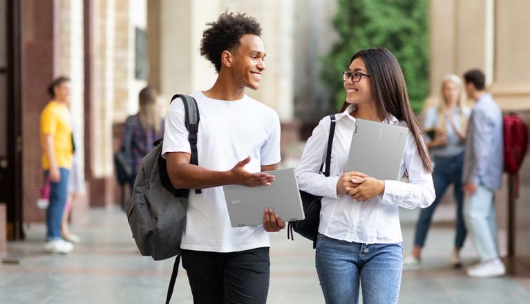 Image of two students chatting and walking, both holding an Acer Chromebook Spin 513