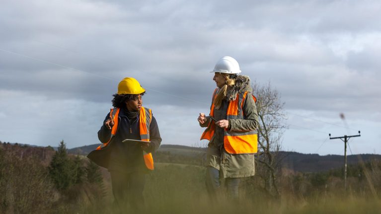 Two women wearing fluorescent jackets talking outside