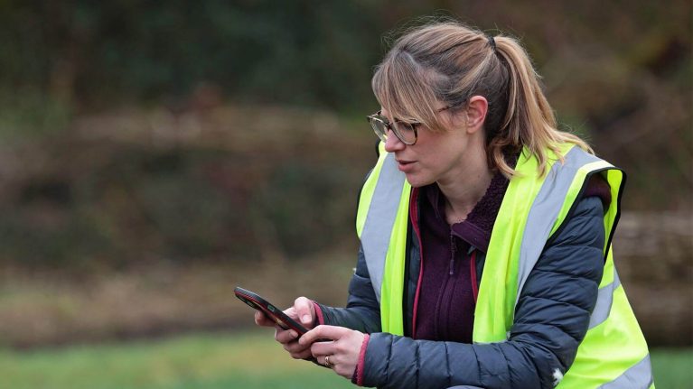 Woman in green fluorescent jacket using her phone outside