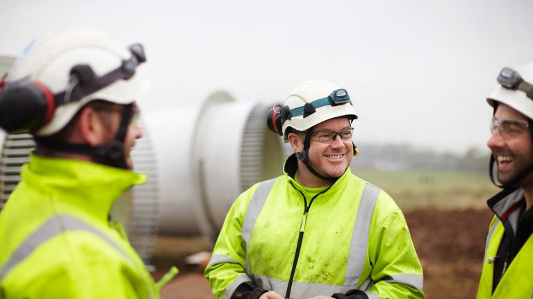 Three engineers in protective gear talking to each other outside