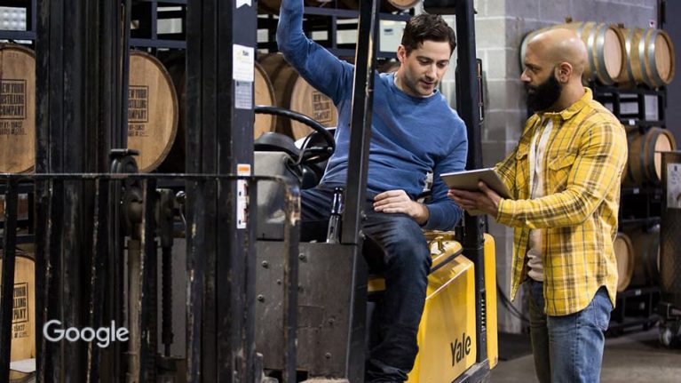 Man on forklift truck with man looking at tablet device